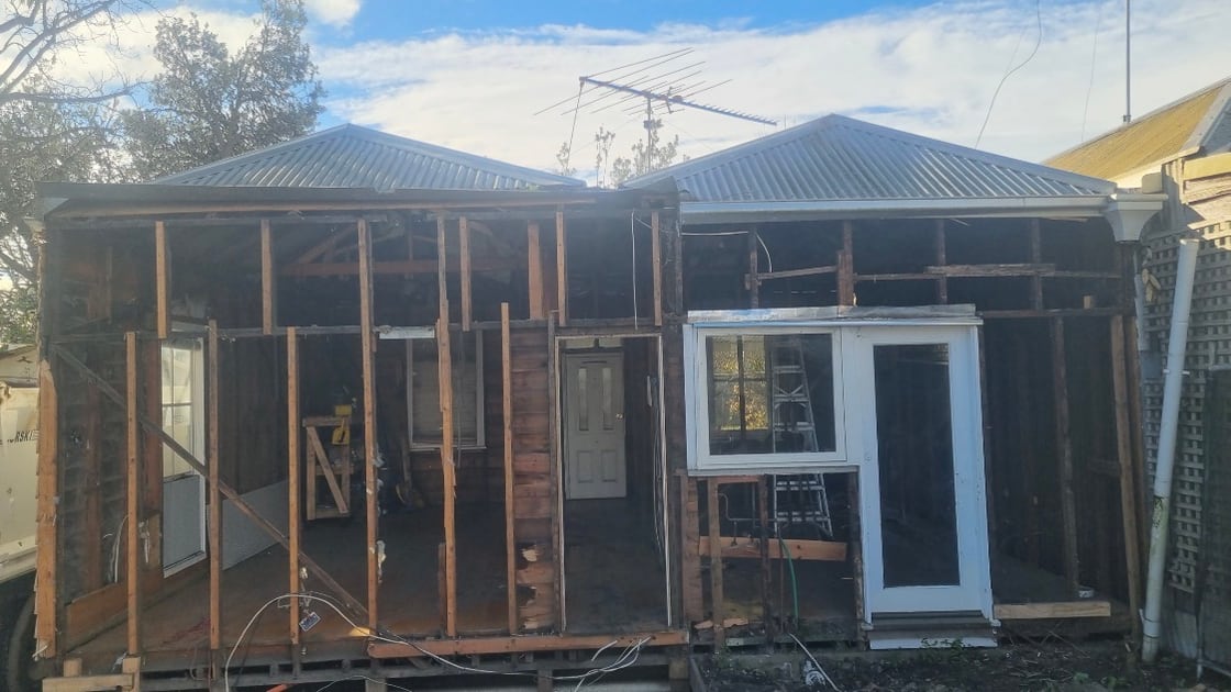 Rear elevation of a weatherboard house with the wall cladding stripped back to bare timber framing and new roof sheeting already fitted